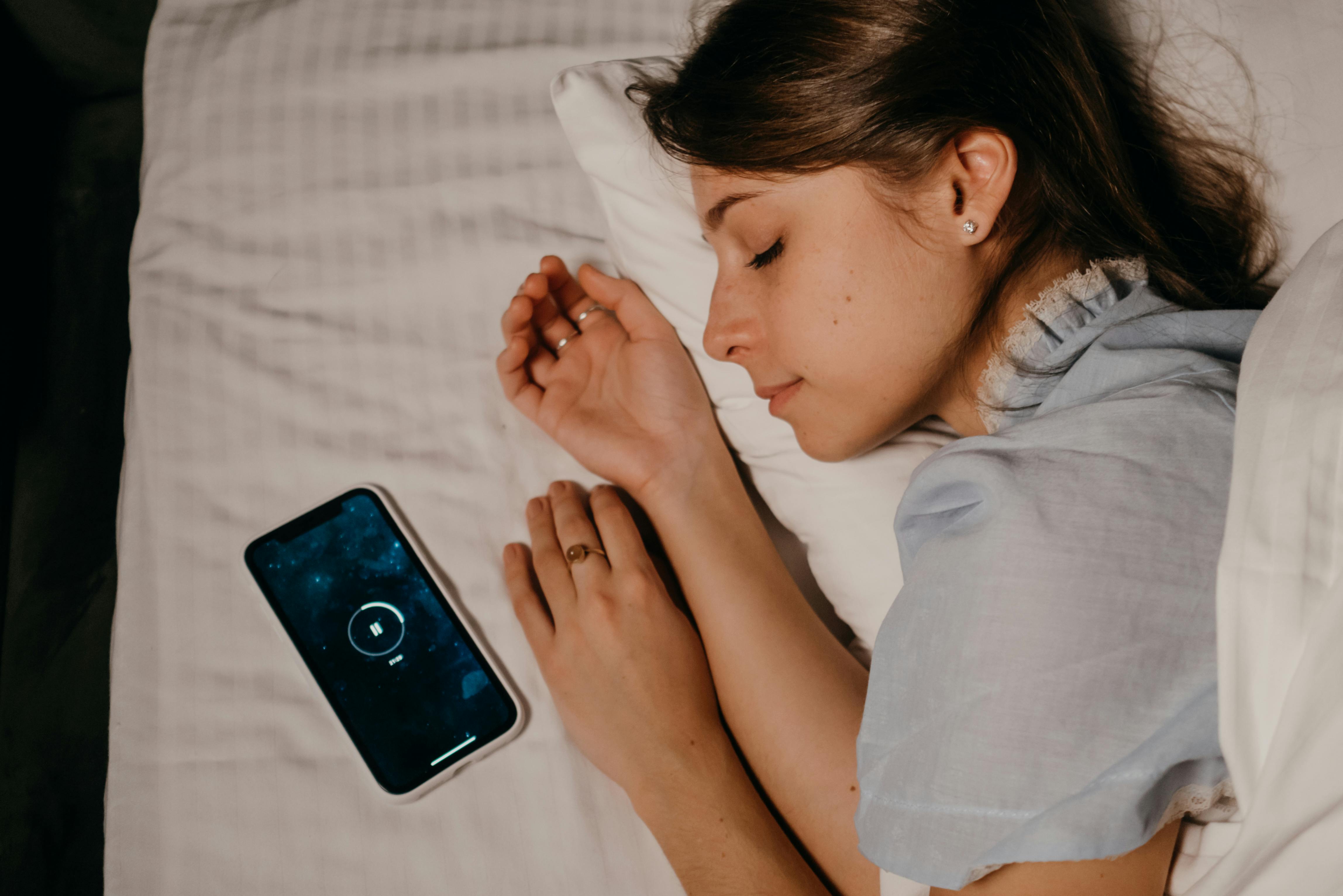 blue-light-detox-evening-cortisol-management.jpg | Calmly Rooted A person sleeping next to a glowing smartphone, illustrating the need for a blue light detox to manage evening cortisol.