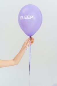 cbd-vs-melatonin-sleep-support-calmly-rooted | Calmly Rooted A hand holding a purple balloon with the word SLEEP for a CBD vs melatonin comparison guide at Calmly Rooted West Bloomfield MI.