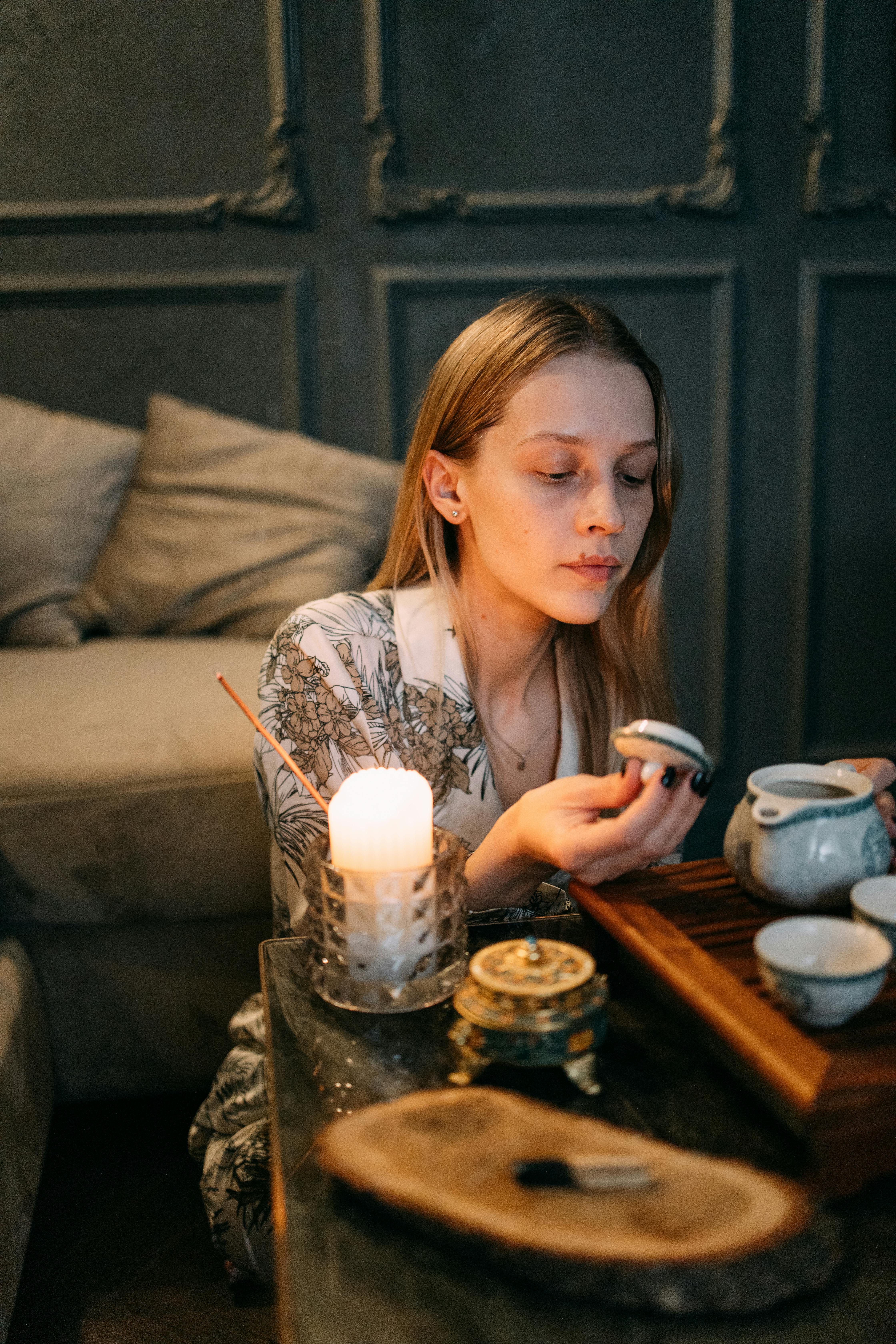 The Sensory Tea Ritual for Nervous System Regulation | Calmly Rooted A woman practicing a mindful tea ritual with a ceramic teapot, incense, and a warm candle to regulate the nervous system and reduce stress.