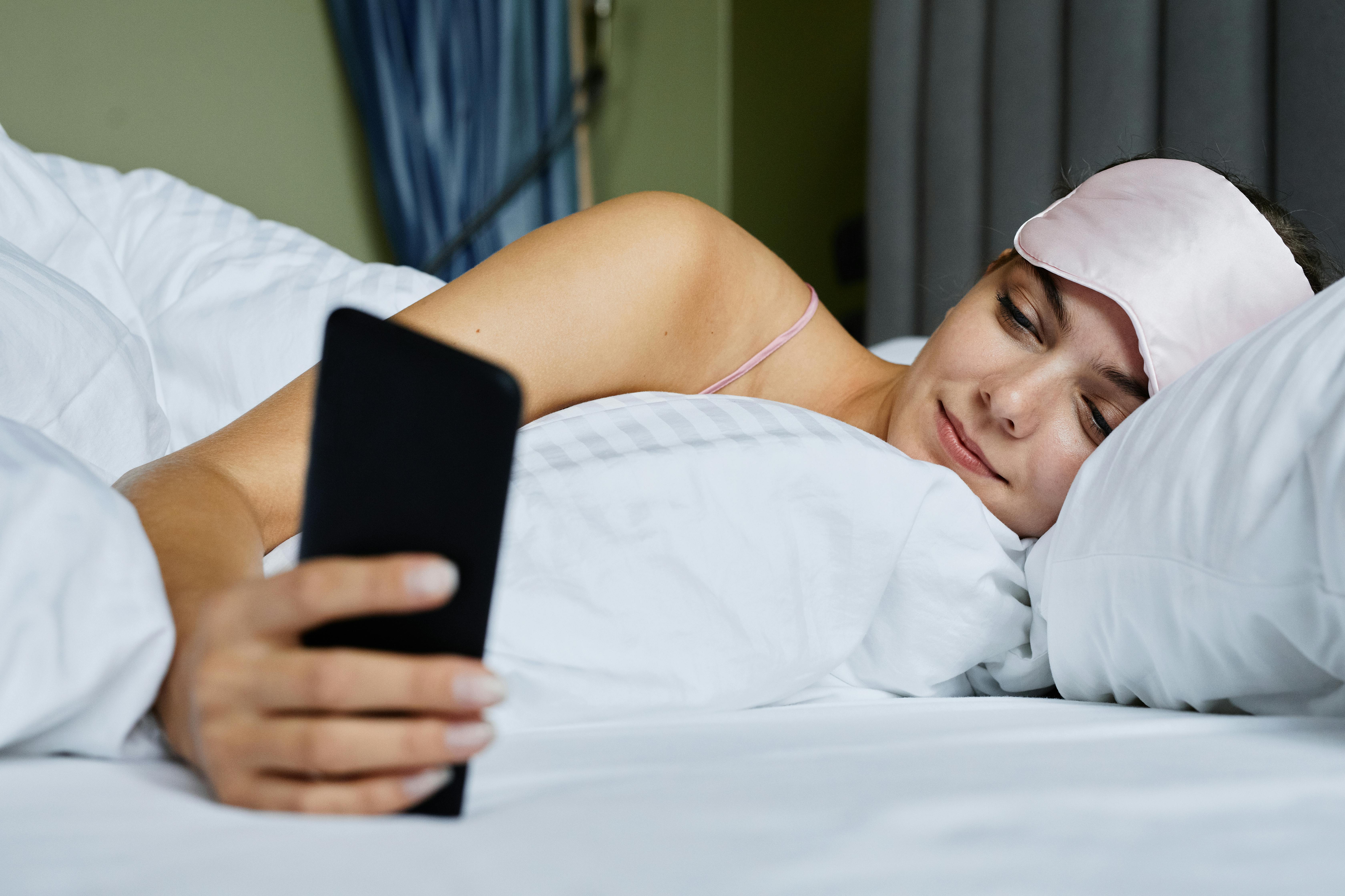 Why Your Deep Sleep Is Low: Real Fixes That Work | Calmly Rooted Woman in bed with a sleep mask checking her phone for deep sleep data and tracker results.