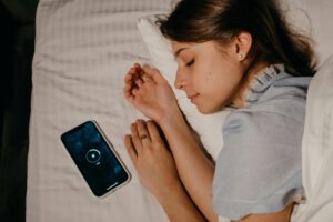 blue-light-detox-evening-cortisol-management.jpg | Calmly Rooted A person sleeping next to a glowing smartphone, illustrating the need for a blue light detox to manage evening cortisol.