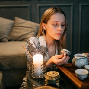 The Sensory Tea Ritual for Nervous System Regulation | Calmly Rooted A woman practicing a mindful tea ritual with a ceramic teapot, incense, and a warm candle to regulate the nervous system and reduce stress.