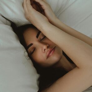 Restorative Sleep with Magnesium Glycinate | Calmly Rooted A woman sleeping peacefully on white linens, illustrating the restorative rest benefits of Magnesium Glycinate for sleep.