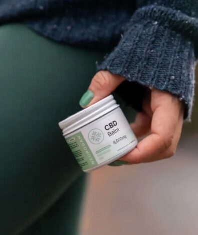 A close-up of a person wearing a cozy green sweater and green leggings holding a jar of extra strength 8000mg CBD relief balm against their leg.