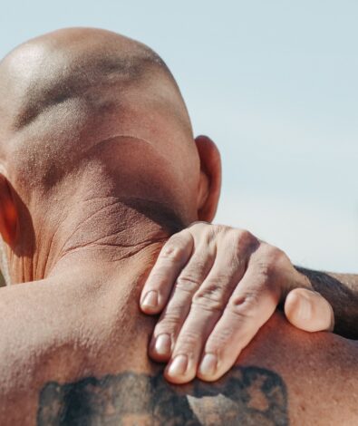 A man massaging his sore neck and shoulder outdoors, representing the need for targeted active recovery and the soothing relief of premium CBD topicals.