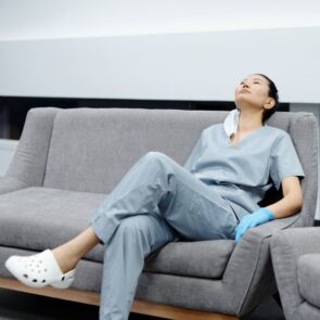 An exhausted person lying in bed trying to sleep while harsh daytime sunlight streams across their face, representing the struggle of shift workers fixing their sleep schedule.