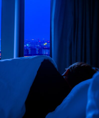 A person lying in bed at night in a dark room overlooking a city, representing the struggle of a racing mind and the need for functional mushrooms for sleep.