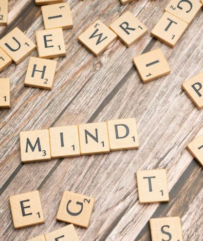 Scrabble tiles scattered on a wooden surface with the word "MIND" spelled out in the center.