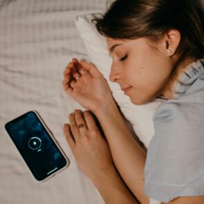 blue-light-detox-evening-cortisol-management.jpg | Calmly Rooted A person sleeping next to a glowing smartphone, illustrating the need for a blue light detox to manage evening cortisol.
