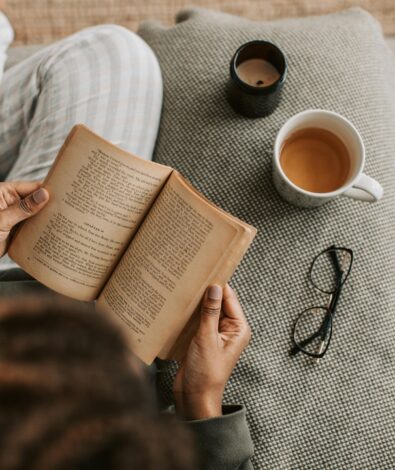 A person relaxing on a textured sofa reading a book next to a warm cup of herbal tea and a candle, practicing a calming evening wind-down ritual.